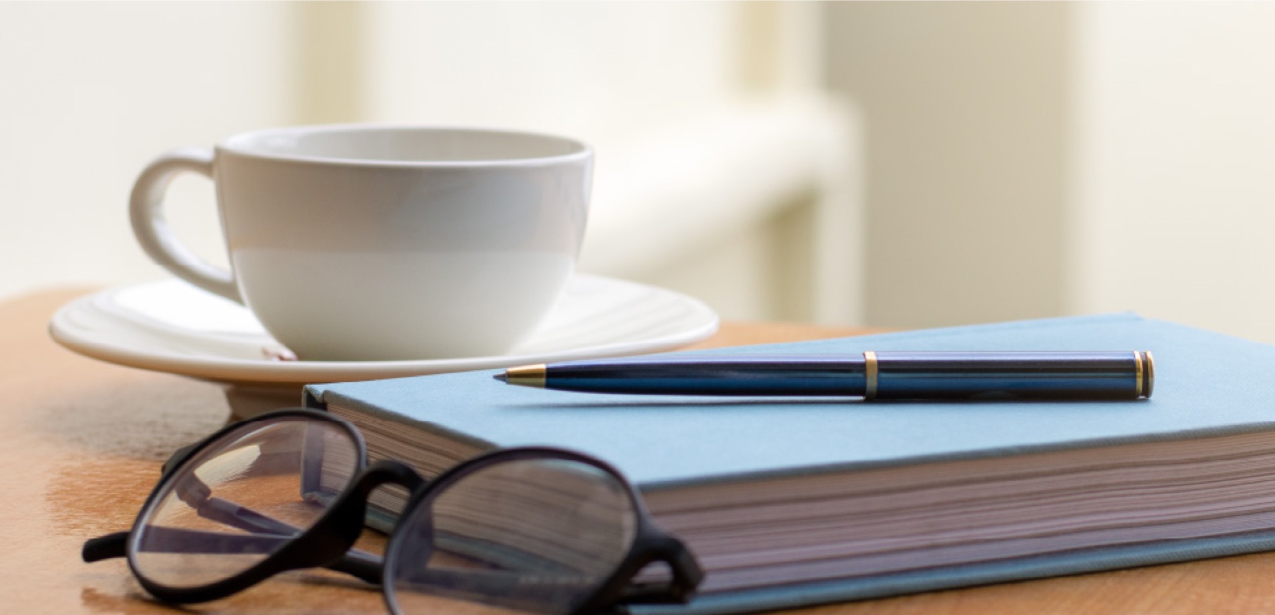 oggetti su tavolo: tazzina, agenda, penna e occhiali
